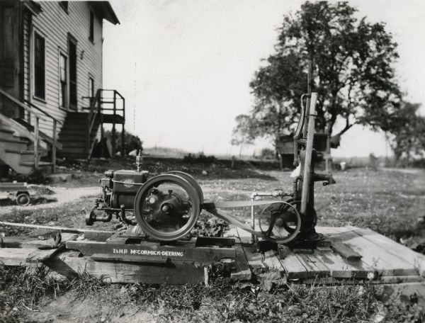 A 1.5 horsepower McCormick-Deering engine powering a water pump outside of a building on International Harvester's Hinsdale experimental farm.