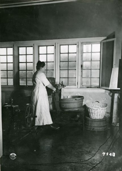 A woman using an electric washer and wringer to launder clothing on the Babcock Farm.