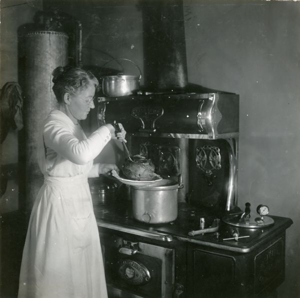 Mrs. Irving Bielby placing a roast on a plate after cooking it in a pressure kettle at the Babcock farm.