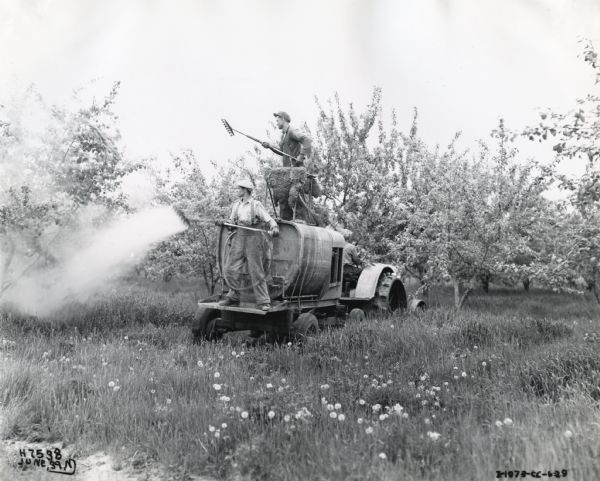 Two men use a 150-gallon sprayer attached to the back of a McCormick-Deering 10-20 tractor to apply pesticide to trees in an orchard.  The photograph was taken in Markham, Ontario, Canada.