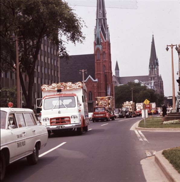 A Sauk County traffic police vehicle leads a line of circus wagons through past two church buildings during a parade originating at Circus World Museum in Baraboo. The 25 circus wagons were carried on the beds of International trucks.