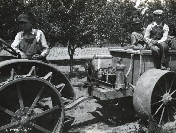 Three men pose on a McCormick-Deering 10-20 tractor outfitted with an orchard sprayer in front of a grove of trees.