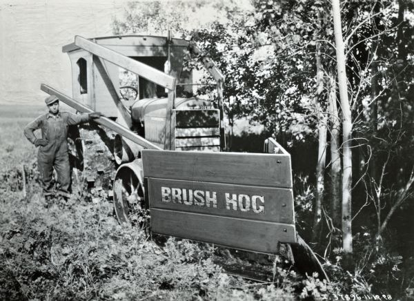 A man stands beside a McCormick-Deering tractor outfitted with a "Brush Hog."