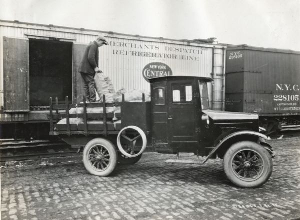 A man loads burlap bags of potatoes from a railroad car onto the back of an International Model S truck owned by Howard Reilley.