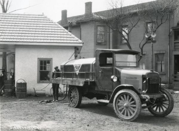 A man filling the oil tank of an International Model 33 truck owned by the Rochester Fuel and Feed Company.