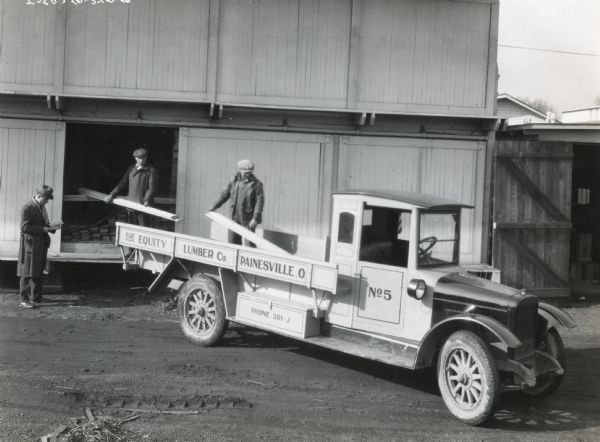 Men loading pieces of lumber onto the bed of an International Model SL truck owned by the Equity Lumber Company.