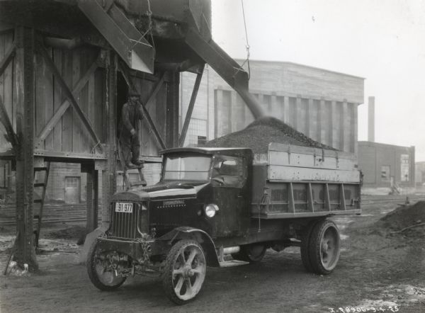An International Model 103 truck with a wood W-12 body and F-6 hoist owned by H. Schwartz, contractor, accepts a load of cinders from a chute.