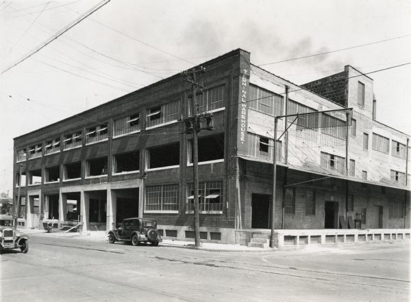Exterior view of the International Harvester Company Little Rock branch. Automobiles are parked along the street in front of the building. The building appears to be under construction, as the lower two floors of the building do not have windows or doors. A man is working near a wheelbarrow on the sidewalk.