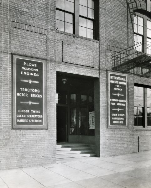 Entrance to International Harvester's San Francisco branch building.  Signs are posted on either side of the doors reading: "Plows, Wagons, Engines. Tractors, Motor Trucks. Binder Twine, Cream Separators, Manure Spreaders" and "International Harvester Company of America. McCormick-Deering Farm Machines. Grain Drills, Harvesting Machines."