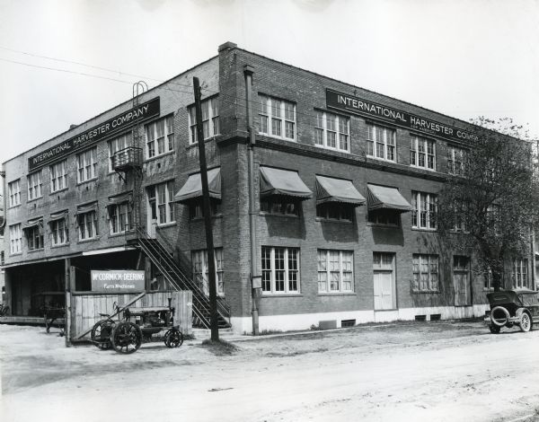 A Farmall tractor and an automobile are parked alongside the curb running past International Harvester Company's Houston branch building. Signs on the building's exterior read: "International Harvester Company (Of America)" and "McCormick-Deering Farm Machines."