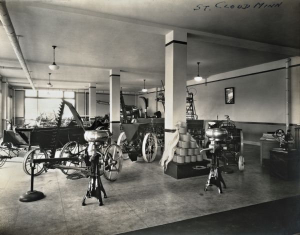 Interior view of a showroom at International Harvester Company's St. Cloud branch building. Cream separators, spools of twine, and various agricultural machinery and implements stand on display.