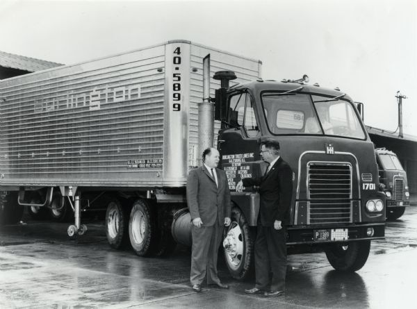 Two men wearing suits are standing outdoors beside an International DCOF-405 truck purchased by Burlington Truck Lines, Inc.