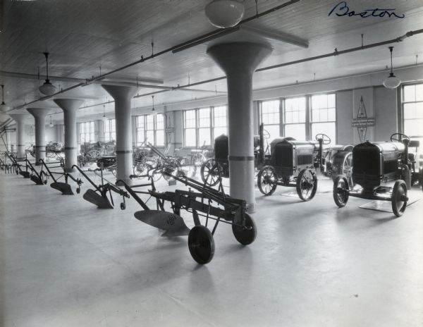 McCormick-Deering tractors, plows, and other agricultural implements are arranged on display in a showroom. A sign advertising cream separators hangs on the wall, reading "McCormick-Deering Primrose Separators. Good equipment makes a good farmer better."