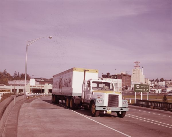 An International DF 405 truck owned by Lucky Lager drives down a highway away. The Lucky Lager factory is in the background.
