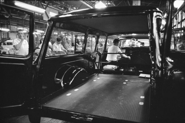 View through a truck body of men at work in an International Motor Truck Division factory, probably the Springfield Works. Other men can be seen working on trucks farther down the assembly line.