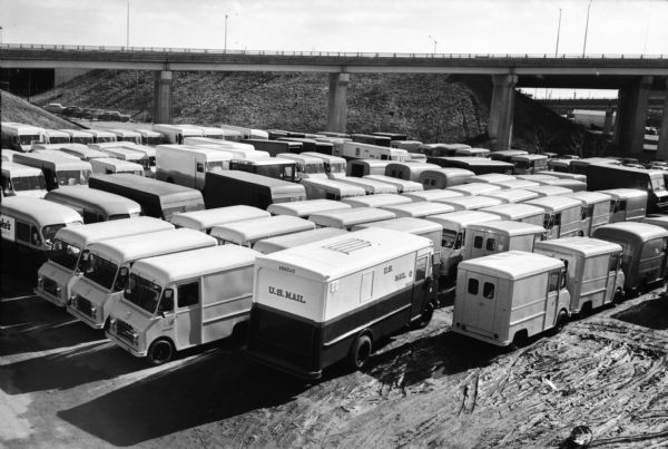 Elevated view of International Metro trucks parked beside a highway overpass. A group of cars are parked in the background on the left.