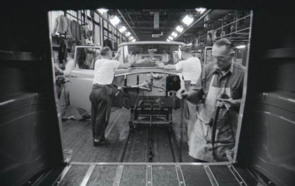 View from interior of truck of factory workers tending to partially-assembled trucks as they move down an assembly line at International Harvester's Springfield Works.