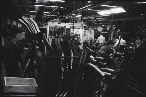 Men work on trucks in an International factory, possibly Springfield Works. Truck parts are piled in the foreground.