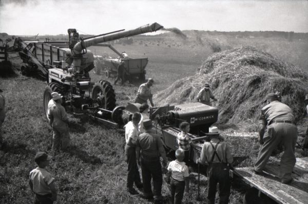 Elevated view of men and boys gathered around a hay baler and other machines at work on International Harvester's Hickory Hill farm. The farm was located 75 miles southwest of Chicago and was kept as a location to photograph and make videos of International Harvester equipment.