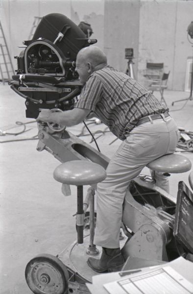 A man uses a motion picture camera while filming in a studio at International Harvester's Hickory Hill Farm.