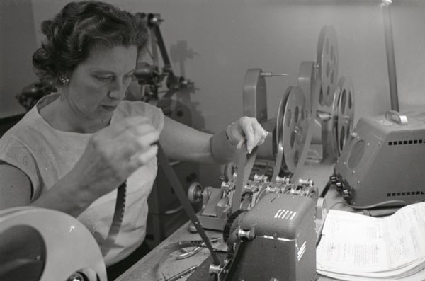 A woman sits at a table while spooling motion picture film onto a reel at International Harvester's Hickory Hill Farm.