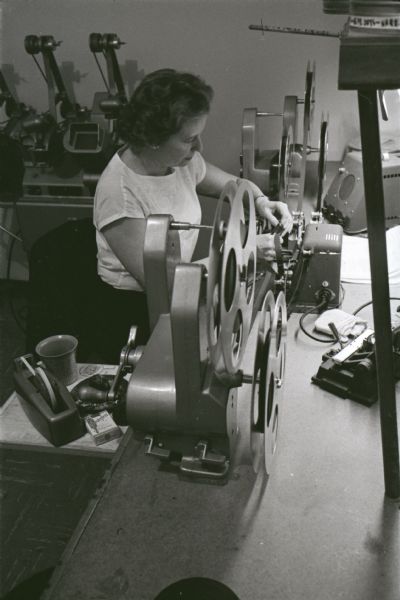 A woman is working at a table while spooling motion picture film onto a reel at International Harvester's Hickory Hill Farm.