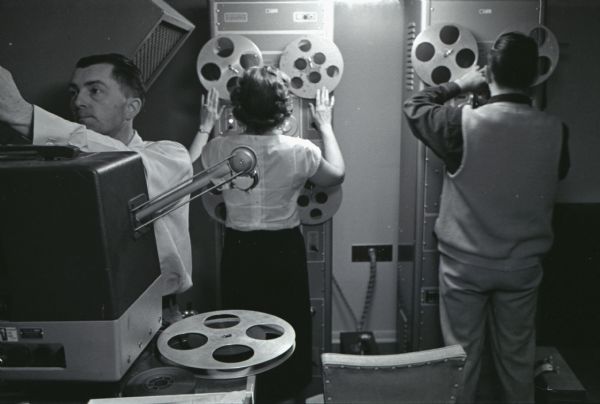 Two men and a woman operate film reels inside a room at International Harvester's Hickory Hill Farm.