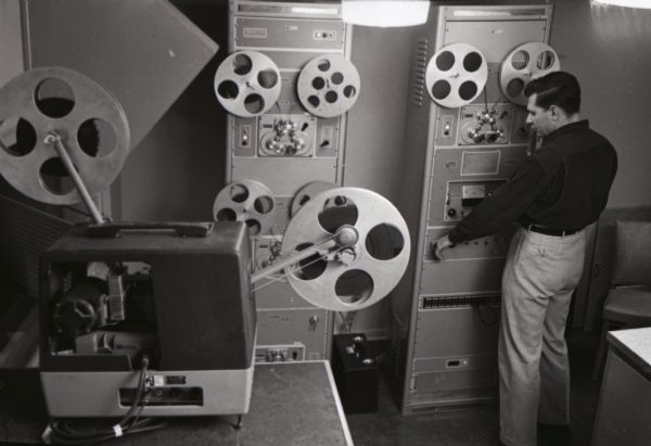 A man operates a film reel inside a room at International Harvester's Hickory Hill Farm.