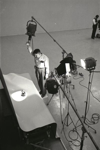 Elevated view of a man adjusting a light at International Harvester's Hickory Hill studio while preparing to photograph a ball bearing for the company's catalog.