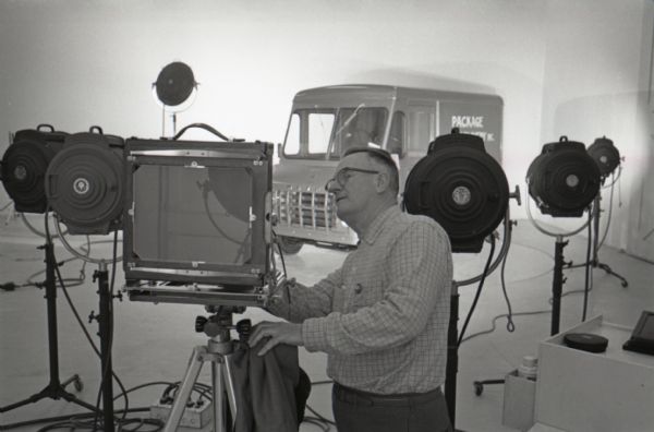 A photographer makes an adjustment to the settings of a view camera in  the studio of International Harvester's Hickory Hill farm while preparing to photograph an International Metro Mite truck.