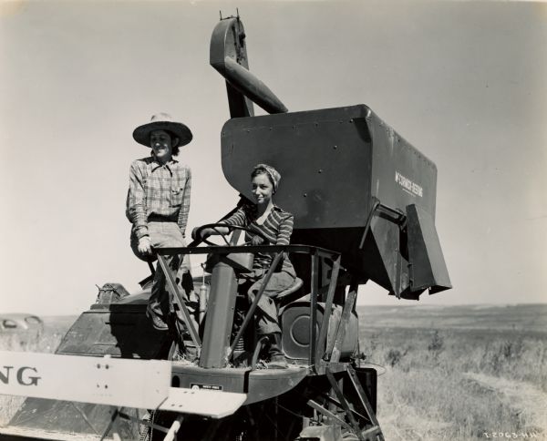 Two women in a field with a McCormick-Deering 123-SP harvester-thresher (combine). An automobile is parked in the background on the left.