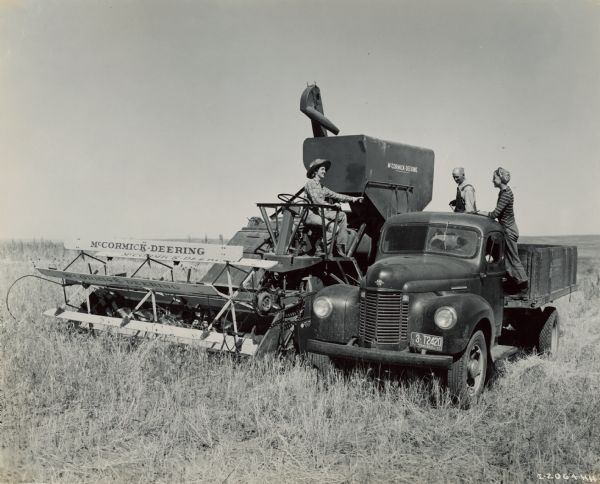 Two women and a man with a McCormick-Deering 123-SP harvester-thresher (combine) and an International truck in a field.