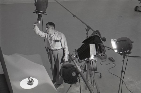 Overhead view of man adjusting lights and a camera as he prepares to photograph a ball bearing for an International Harvester catalog at the company's Hickory Hill Farm.