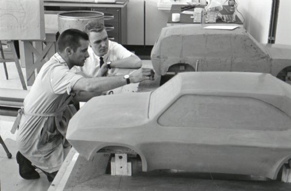 Two men kneel before clay models of a "Multipurpose Safety Utility Vehicle" set on a table during the first styling seminar at the Fort Wayne motor truck engineering department. The program lasted ten weeks and participants were college students in their junior year.