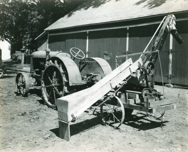 The back of a McCormick-Deering 10-20 tractor with an unidentified harvesting implement attached to the back. A farm building is in the background. A handwritten note under the photograph reads, "Milo G. Clow, Cherokee, KY."