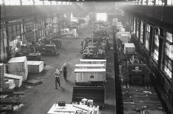 Elevated view of men walking among crawler tractors (TracTracTors)  inside an International Harvester factory, possibly Tractor Works.