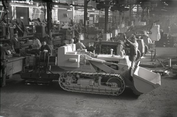 Men work on crawlers inside an International Harvester factory, possibly Tractor Works.