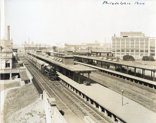 Elevated view of a train stopped at the North Philadelphia depot, surrounded by various industrial buildings, including the International Harvester Company branch house at right.