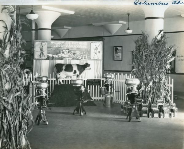 A McCormick-Deering cream separator display stands in a showroom at International Harvester's Columbus branch house. A miniature cow statuette accents a banner advertising McCormick-Deering Ball-Bearing Cream Separators, and oil cans, cream separators, and stalks of wheat decorate the scene.