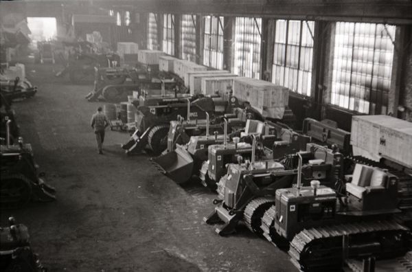 Elevated view of a man walking down a dirt aisle between rows of International Harvester crawler tractors (TracTracTors) in a factory - most likely Tractor Works.