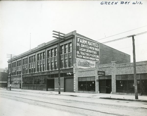 Exterior view of an International Harvester Green Bay branch office building. What appears to be an Auto Wagon and other automobiles are in the display windows of the single-story building at right.
