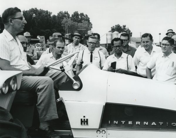 A group of men gathered around an International Harvester HT-340 experimental research tractor that a man is driving.