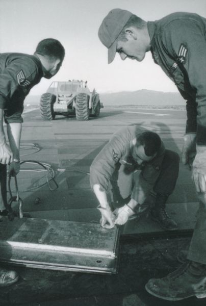 Three men of the Air Force Red Horse heavy repair squad make adjustments to the runway at Phan Rang, a South Vietnam airbase. An International pay scraper is in the background.