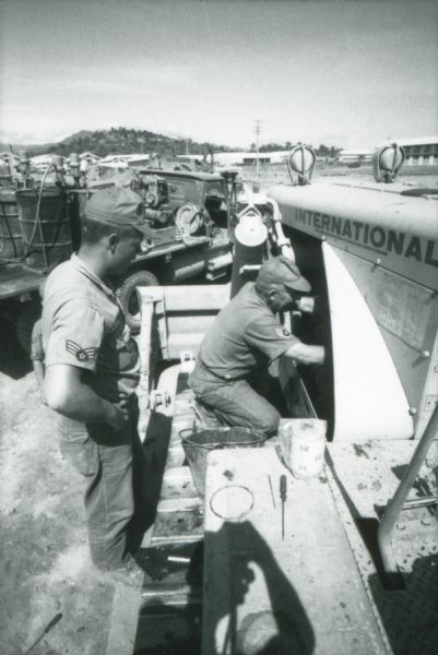 Two men work on an International bulldozer(?) or crawler tractor at the Phan Rang air force base in Vietnam.