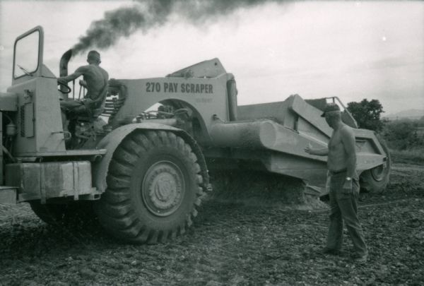 Two men use an International 270 pay scraper while completing construction work at Phan Rang, a South Vietnam air base.