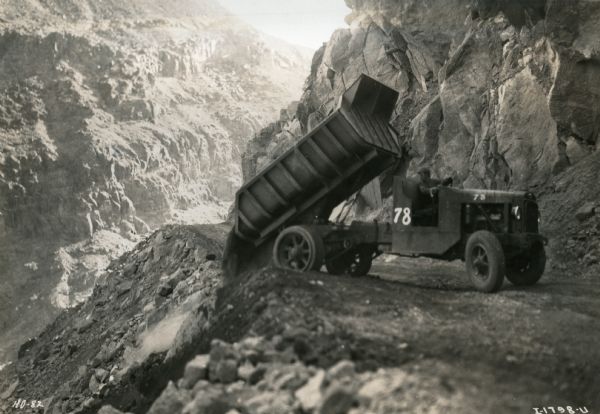 An International dump truck empties its load down the side of a canyon during the construction of the Hoover Dam.