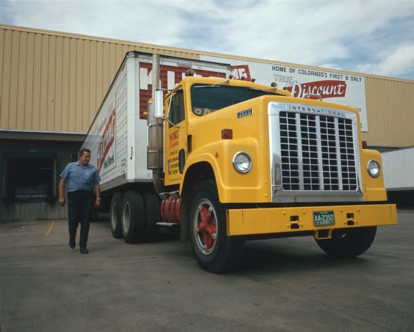 View towards a man walking beside an International Transtar 4200 truck parked in the loading zone of a building or warehouse operated by King Soopers of Denver, Colorado.