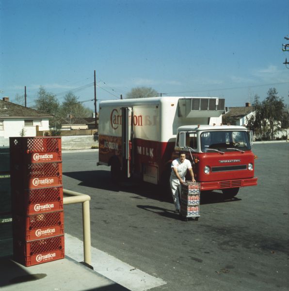 View of a man unloading cartons of milk from an International truck used by the Carnation Company. The truck appears to be an International 1710 COE truck. Milk crates are in the foreground.