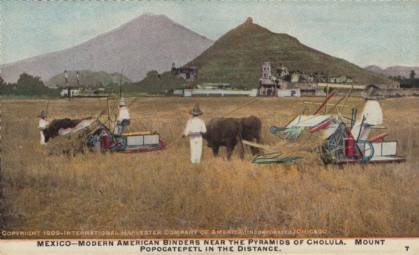 Postcard distributed by International Harvester Company featuring a color illustration of a harvesting scene: four people in the fields of Mexico operating two grain binders pulled by cattle or oxen. Original caption reads: "Mexico — Modern American binders near the pyramids of Cholula. Mount Popocatepetl in the distance."