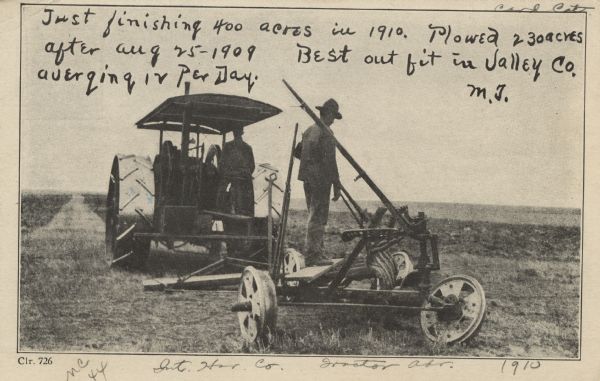 Black and white postcard featuring a photograph of two men. One man is on a tractor, the other is standing on a plow. There is handwriting on the top of the postcard which reads: "Just finishing 400 acres in 1910. Plowed 230 acres after Aug. 25-1909. Best out fit in Valley Co. averaging 12 per day. -M.J."